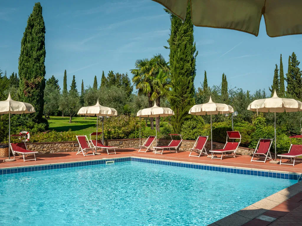  The outdoor pool with sun loungers and parasols, framed by cypresses and olive trees