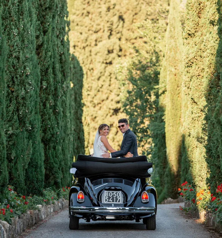  Newlyweds posing on the driveway in a convertible Beetle