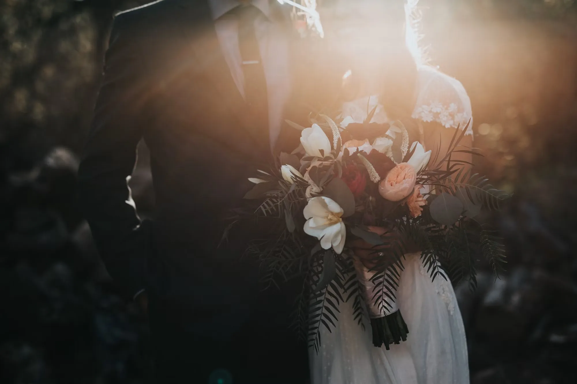  Bride and groom outdoors at sunset, backlit, holding a bouquet